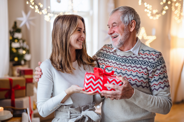 Happy senior man with young woman indoors at home at Christmas, holding present.