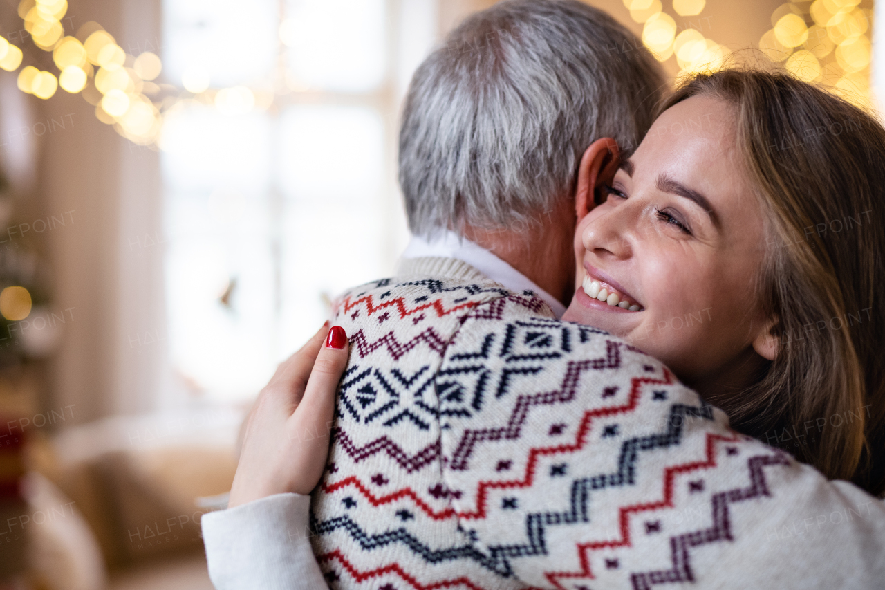 Laughing senior man with young woman indoors at home at Christmas, hugging.