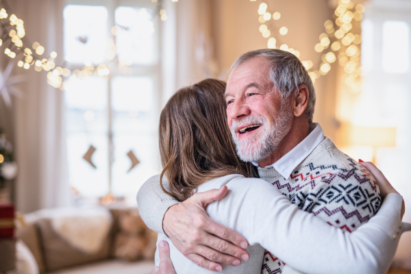 Laughing senior man with young woman indoors at home at Christmas, hugging.