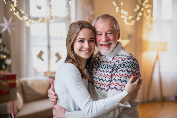 Laughing senior man with young woman indoors at home at Christmas, hugging.