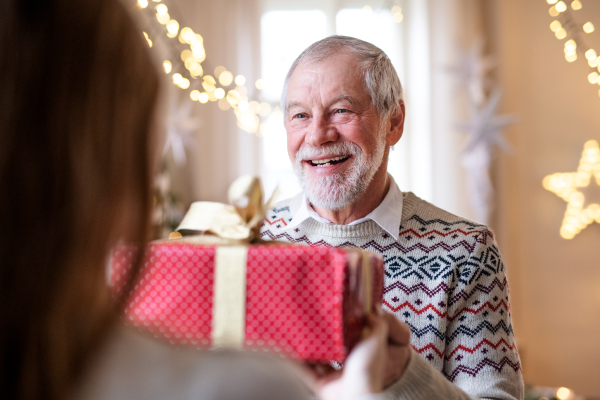 Happy senior man giving present to unrecognizable woman indoors at home at Christmas.