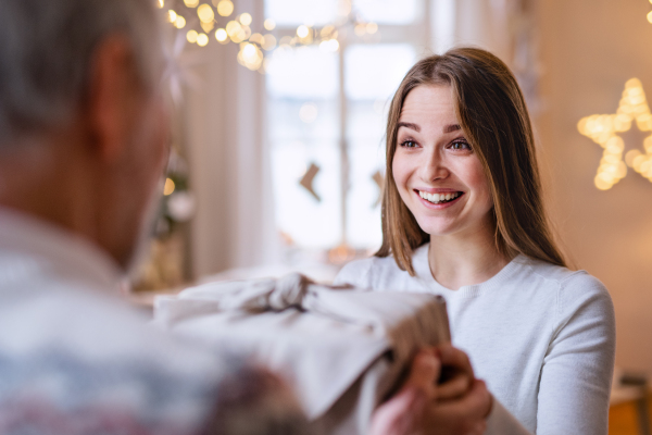 Surprised young woman receiving present from unrecognizable grandfather indoors at home at Christmas.