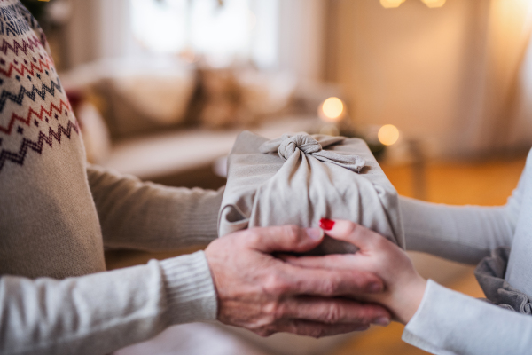 Unrecognizabe woman giving present to senior man indoors at home at Christmas, close-up of hands holding box.