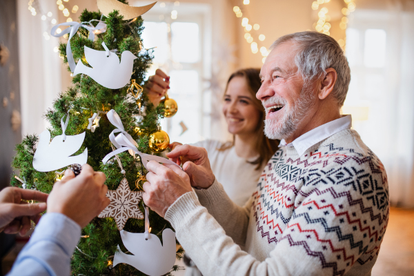 Cheerful multi-generation family indoors at home at Christmas, decorating tree.