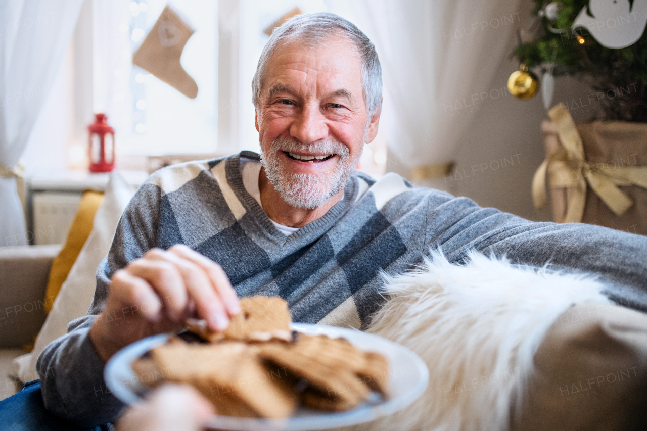 Portrait of happy senior man indoors at home at Christmas, eating biscuits.