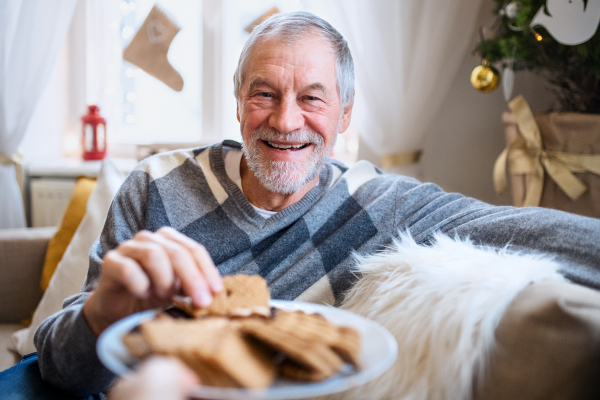 Portrait of happy senior man indoors at home at Christmas, eating biscuits.