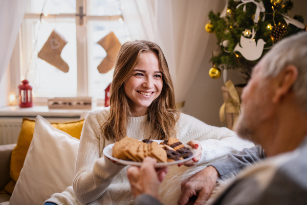 Portrait of young woman with grandfather indoors at home at Christmas, eating biscuits.