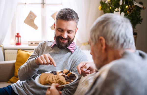 Portrait of mature man and senior father indoors at home at Christmas, eating biscuits.