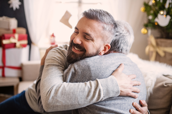 Happy mature man and senior father indoors at home at Christmas, hugging.