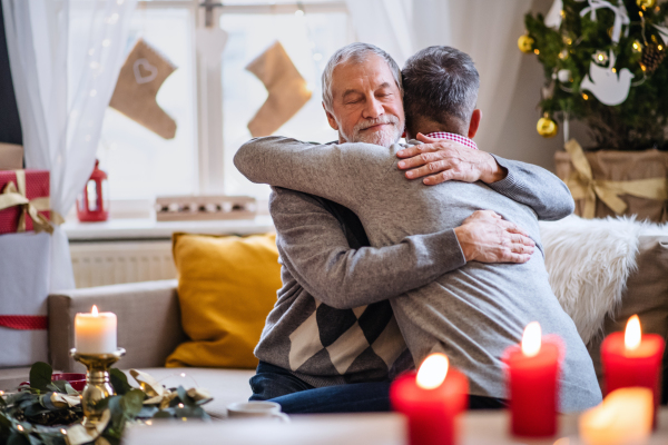 Happy mature man and senior father indoors at home at Christmas, hugging.