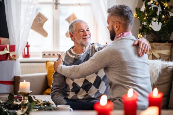 Happy mature man and senior father indoors at home at Christmas, hugging.