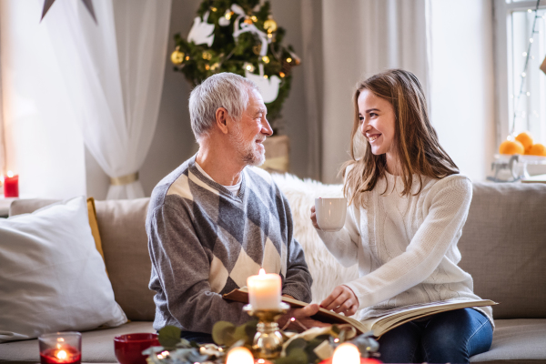 Portrait of young woman with grandfather indoors at home at Christmas, looking at photo album.