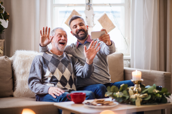 Portrait of mature man and senior father with smartphone indoors at home at Christmas, video call concept.