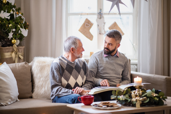 Happy mature man and senior father indoors at home at Christmas, looking at photographs.