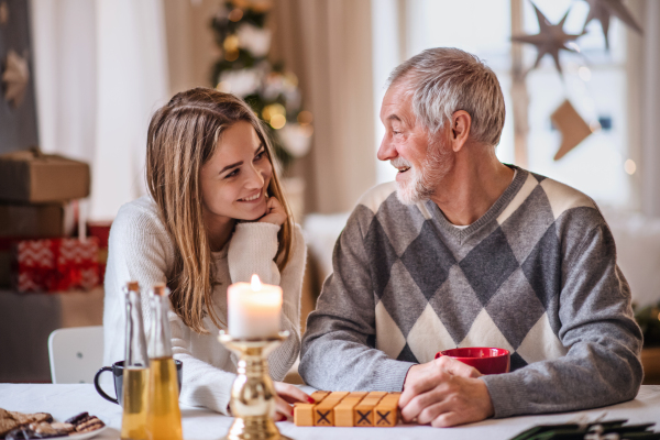 Portrait of young woman with grandfather indoors at home at Christmas, playing board games.