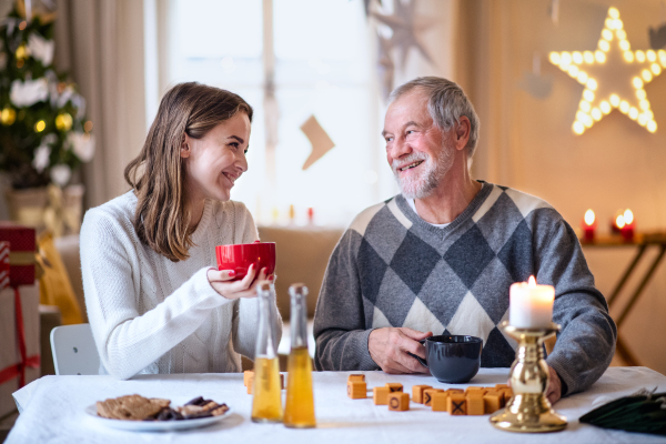 Portrait of young woman with grandfather indoors at home at Christmas, playing board games.