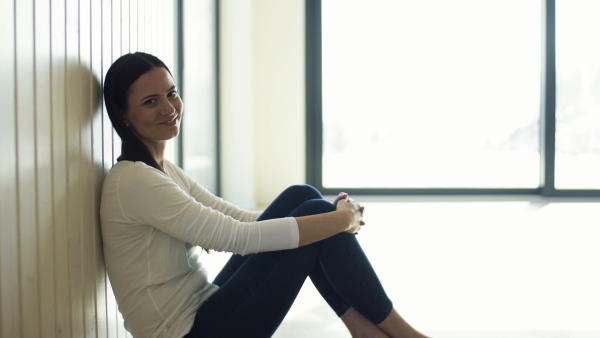 A cheerful young woman sitting on the floor in new home, resting. A moving in new home concept.