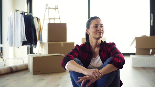 A young cheerful woman furnishing new house, sitting on floor and resting. A moving in new home concept.