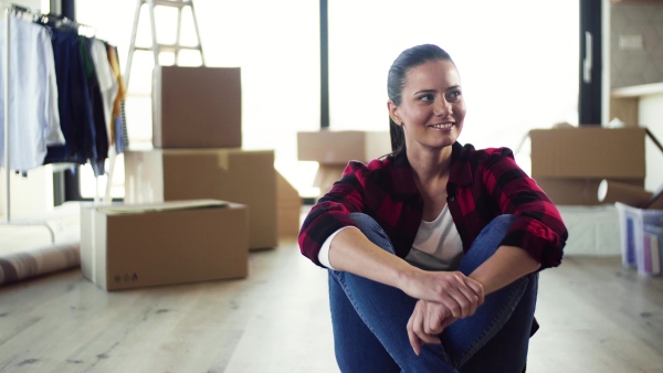 A young cheerful woman furnishing new house, sitting on floor and resting. A moving in new home concept.