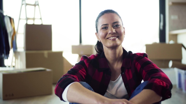 A young cheerful woman furnishing new house, sitting on floor and resting. A moving in new home concept.