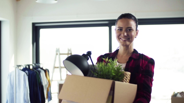 A young happy woman furnishing new house, carrying a box. A moving in new home concept.