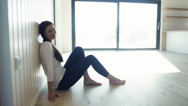 A cheerful young woman sitting on the floor in new home, resting. A moving in new home concept.