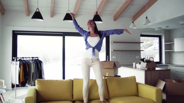 A young woman standing on sofa and dancing. A moving in new home concept.