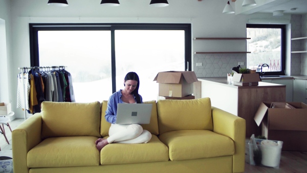 A young woman moving in new home, sitting on sofa and using laptop. A moving in new home concept.