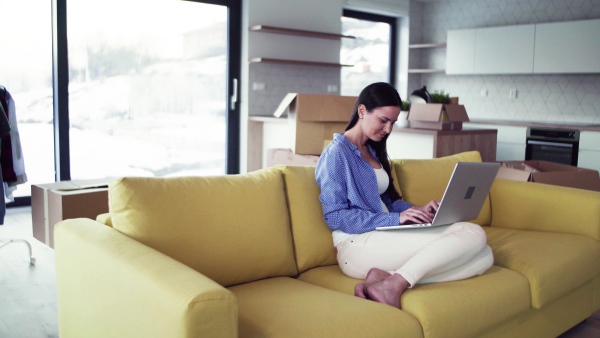 A young woman moving in new home, sitting on sofa and using laptop. A moving in new home concept.