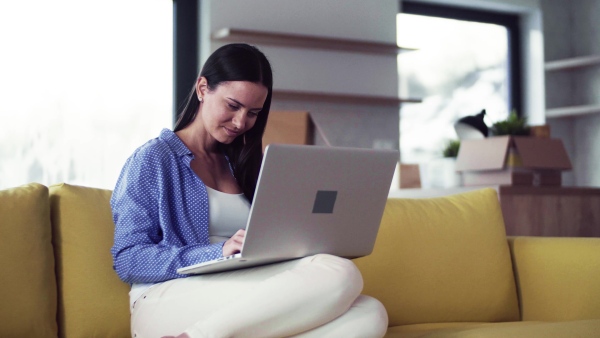 A young woman moving in new home, sitting on sofa and using laptop. A moving in new home concept.