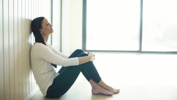 A young woman with closed eyes sitting on the floor in new home, resting. A moving in new home concept. Slow motion.