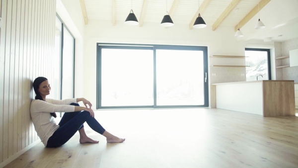 A cheerful young woman sitting on the floor in new home, resting. A moving in new home concept. Slow motion.