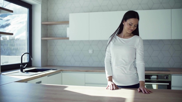 A happy young woman standing in kitchen in new home, resting. A moving in new home concept. Slow motion.