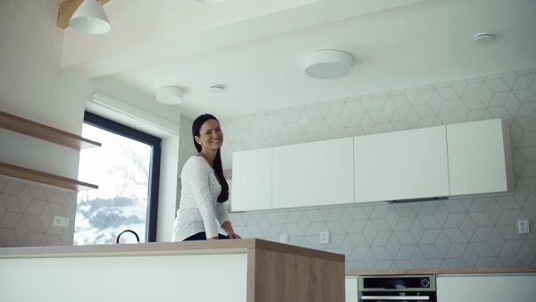 A cheerful young woman sitting on kitchen counter in new home, resting. A moving in new home concept. Slow motion.