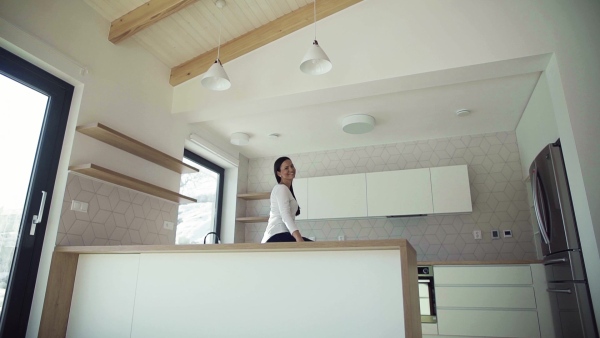 A cheerful young woman sitting on kitchen counter in new home, resting. A moving in new home concept. Slow motion.