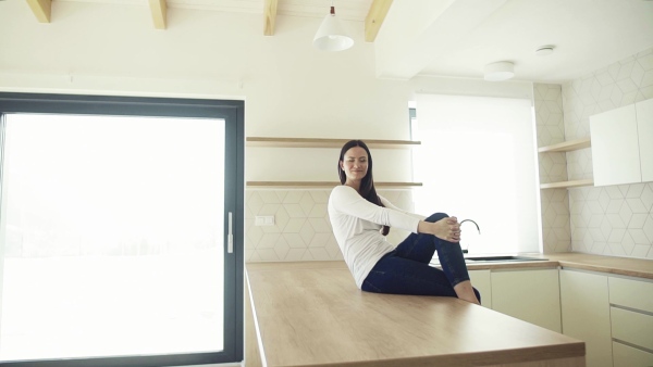 A cheerful young woman sitting on kitchen counter in new home, resting. A moving in new home concept. Slow motion.