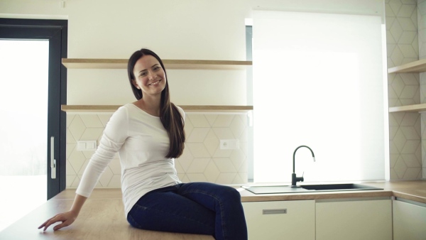 A cheerful young woman sitting on kitchen counter in new home, resting. A moving in new home concept. Slow motion.