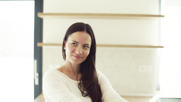 A cheerful young woman sitting on kitchen counter in new home, resting. A moving in new home concept. Slow motion.