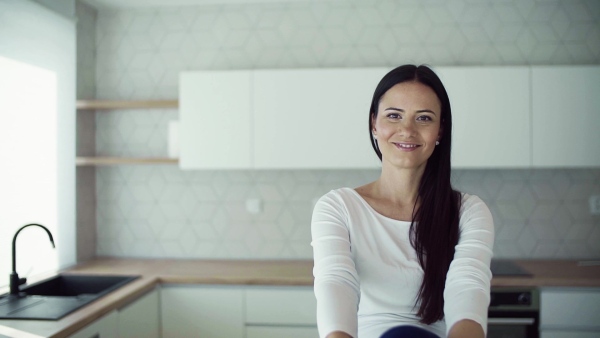 A cheerful young woman sitting on kitchen counter in new home, resting. A moving in new home concept. Slow motion.