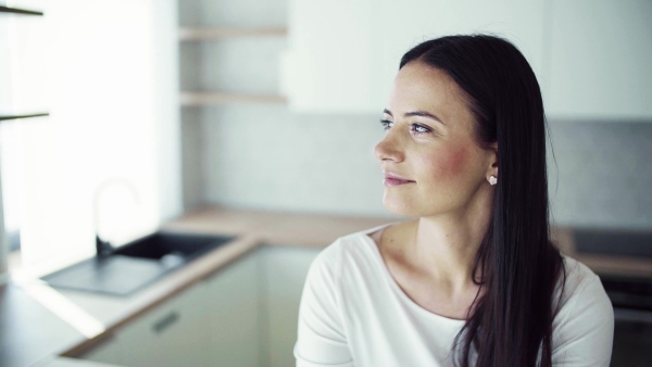 A happy young woman sitting on kitchen counter in new home, resting. A moving in new home concept. Slow motion.