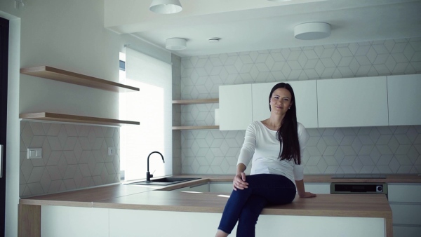 A cheerful young woman sitting on kitchen counter in new home, resting. A moving in new home concept. Slow motion.