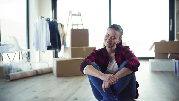 A young cheerful woman furnishing new house, sitting on floor and resting. A moving in new home concept. Slow motion.