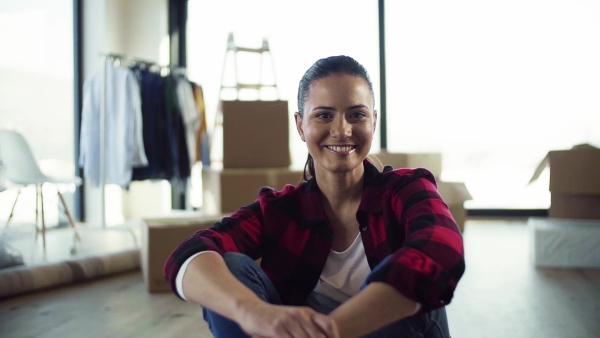 A young cheerful woman furnishing new house, sitting on floor and resting. A moving in new home concept. Slow motion.