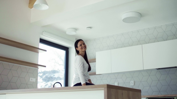 A cheerful young woman leaning on kitchen counter in new home, resting. A moving in new home concept.