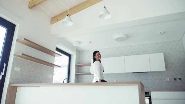 A cheerful young woman leaning on kitchen counter in new home, resting. A moving in new home concept.