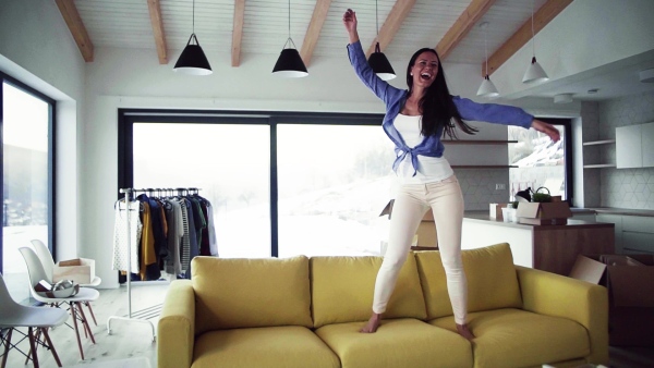 A young woman standing on sofa and dancing. A moving in new home concept. Slow motion.