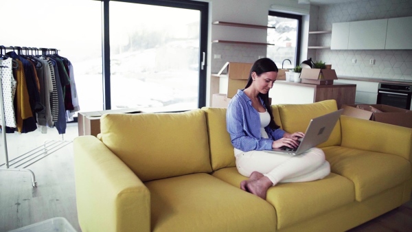 A young woman moving in new home, sitting on sofa and using laptop. A moving in new home concept. Slow motion.