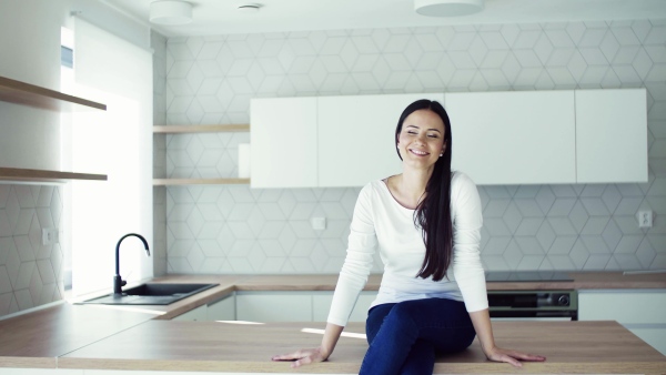 A cheerful young woman sitting on kitchen counter in new home, resting. A moving in new home concept.