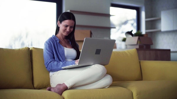 A young woman moving in new home, sitting on sofa and using laptop. A moving in new home concept. Slow motion.