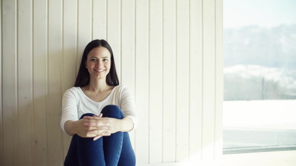 A cheerful young woman sitting on the floor in new home, resting. A moving in new home concept. Slow motion.